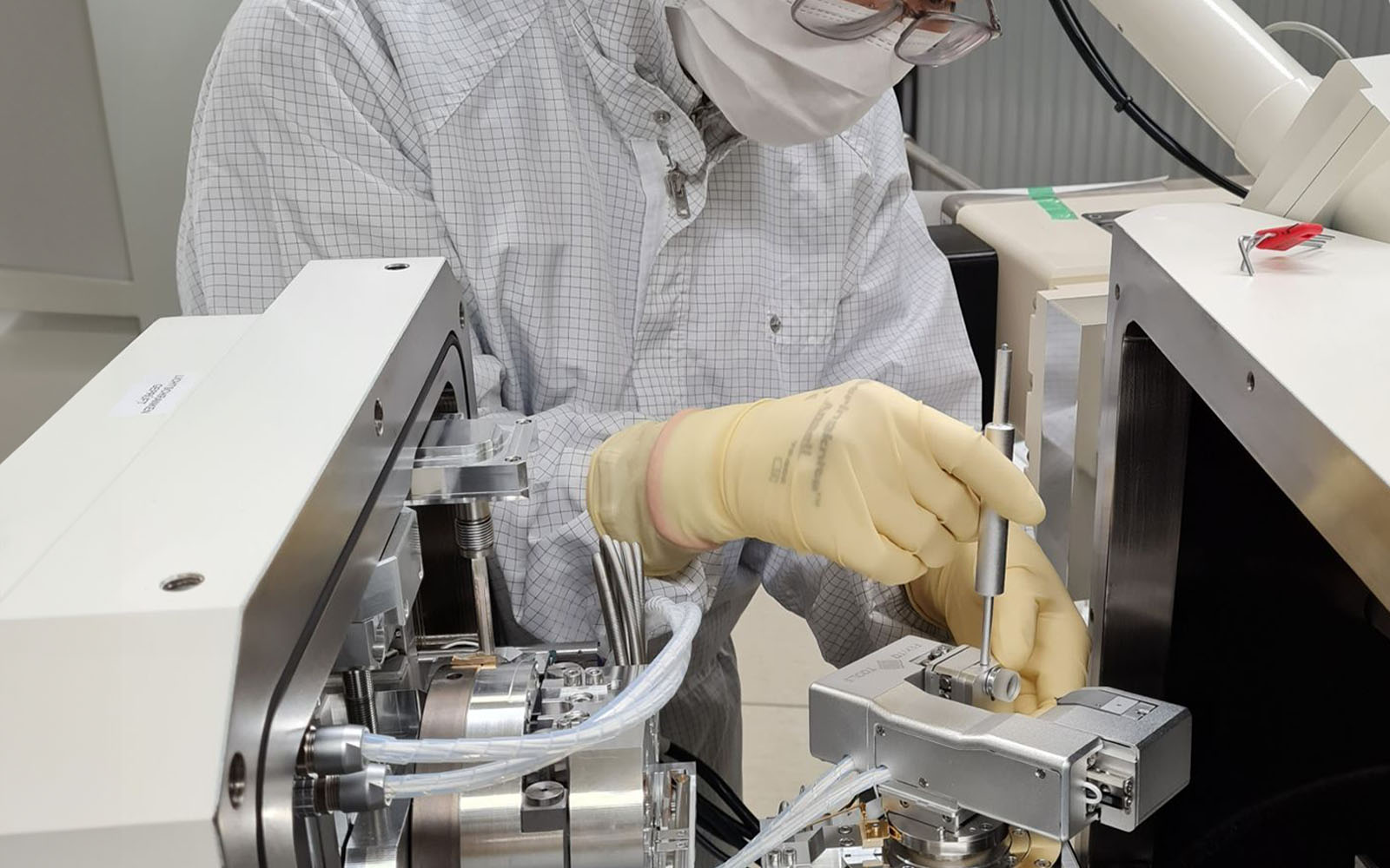 <p>Technician in cleanroom suit installing NMT04 nanoindenter in a SEM.</p>